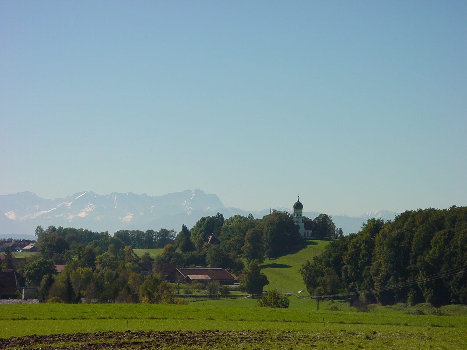 Blick über die Wiesen zur Holzhauser Kirche mit Alpenkette