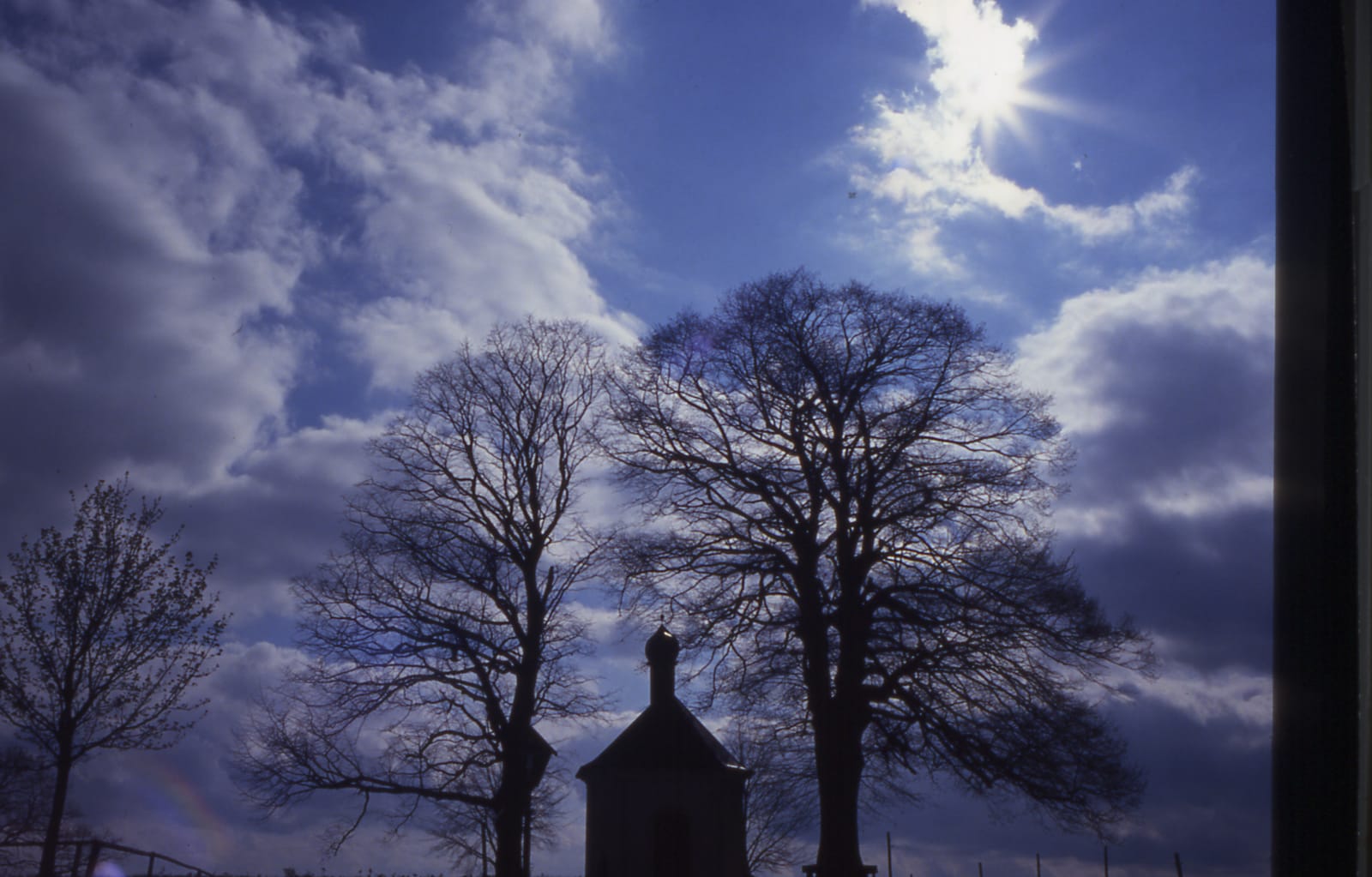 Kapelle mit Lindengruppe unter dramatischem Wolkenhimmel (Dia-Scan)