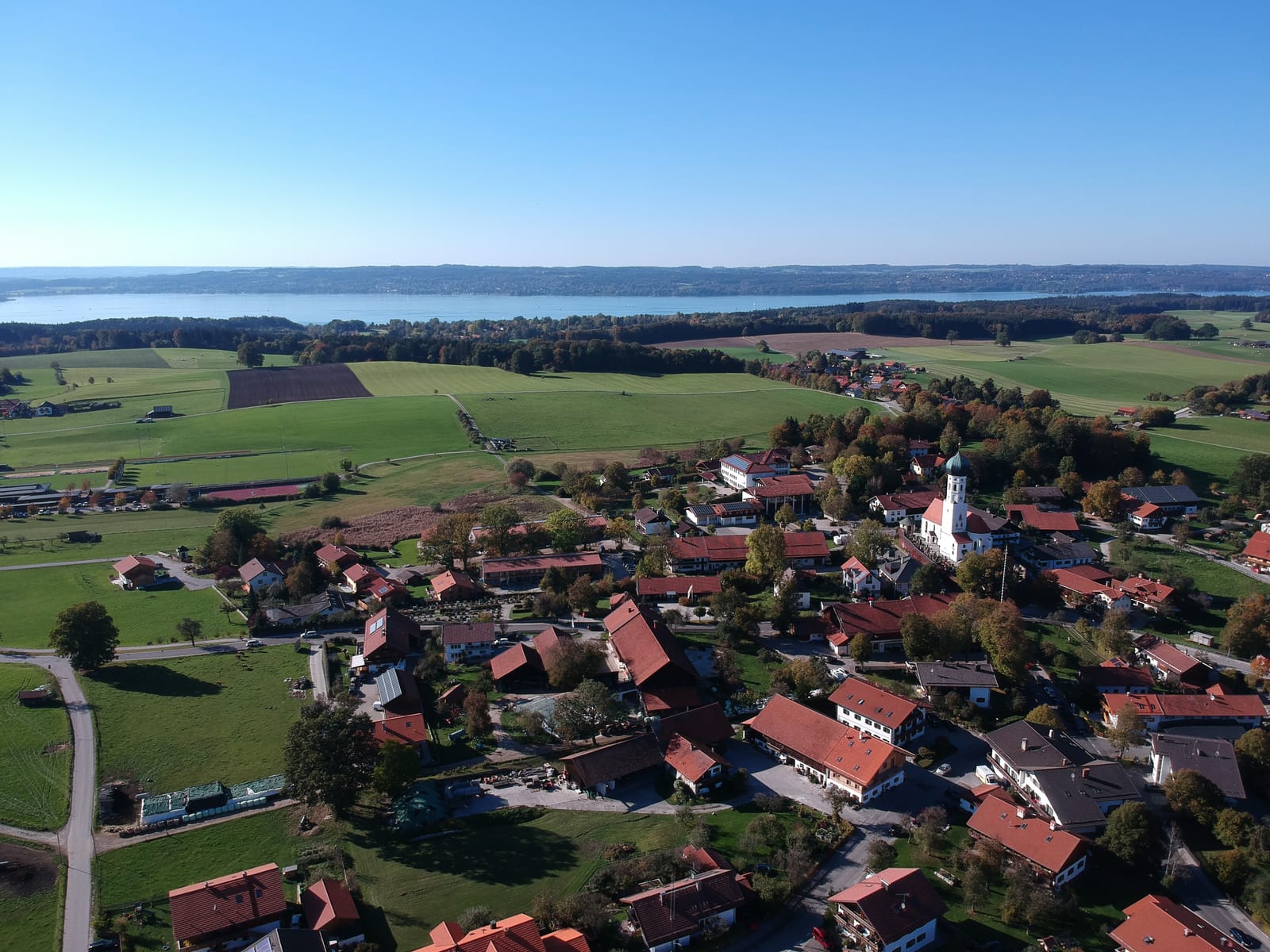 Luftbild des Ortes mit Kirche, See und Voralpenland
